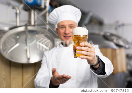 Brewmaster holding out glass of fresh foamy pale ale 96747813