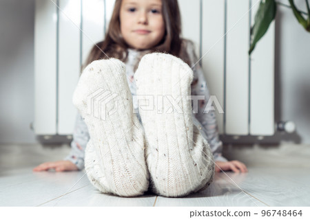 Closeup, focus on smiling, calm girl feet in white woolen socks, showing to camera, sitting near heat radiator at home Closeup, focus on smiling, calm girl feet in white woolen socks, showing to camera, sitting near heat radiator at home 96748464