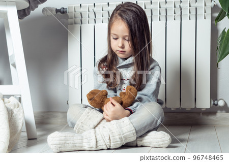 Calm independent nice little girl warming up near heating radiator and play with stuffed soft bear toys and having fun Calm independent nice little girl warming up near heating radiator and play with stuffed soft bear toys and having fun 96748465