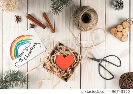 Open fabric present box with red heart craft, rainbow card merry christmas. DIY, handmade gifts with scissors. Flat lay Open fabric present box with red heart craft, rainbow card merry christmas. DIY, handmade gifts with scissors. Flat lay 96748500