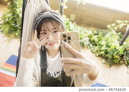 一位年輕女子睡在吊床上,用智能手機自拍 Home Camping Camping Image 一位年輕女子睡在吊床上,用智能手機自拍 Home Camping Camping Image 96748826