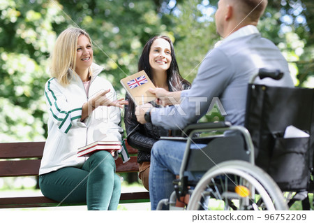 Three friends talk and study outdoors, one disabled person in wheelchair. Three friends talk and study outdoors, one disabled person in wheelchair. 96752209