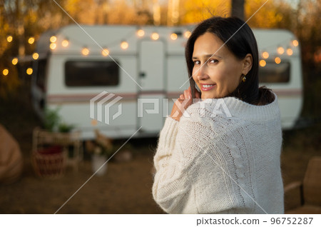 A pensive Caucasian woman in a white knitted sweater is resting in a warm autumn near a motorhome. Travel by camper. A pensive Caucasian woman in a white knitted sweater is resting in a warm autumn near a motorhome. Travel by camper. 96752287