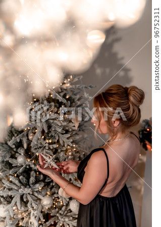 Portrait of a wealthy mature woman with evening makeup and hairstyle posing in a black dress against the backdrop of a Christmas room. Luxurious lifestyle. Cosmetology, plastic surgery, rejuvenation. Portrait of a wealthy mature woman with evening makeup and hairstyle posing in a black dress against the backdrop of a Christmas room. Luxurious lifestyle. Cosmetology, plastic surgery, rejuvenation. 96752311