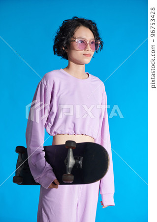 Portrait of teenage girl with skateboard standing against blue background 96753428