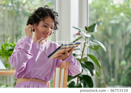 Cheerful girl putting in earbuds to watch movie on tablet computer 96753539