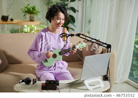 Cheerful teenage girl enjoying playing ukulele and singing 96753552