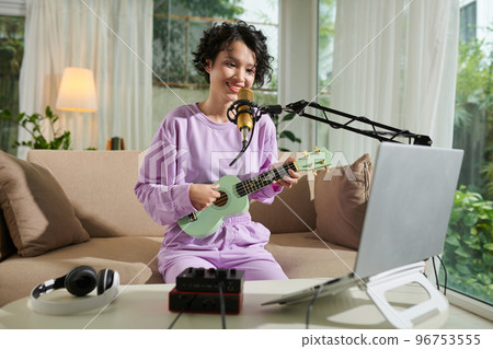 Smiling teenage girl singing in mike and playing ukulele Smiling teenage girl singing in mike and playing ukulele 96753555