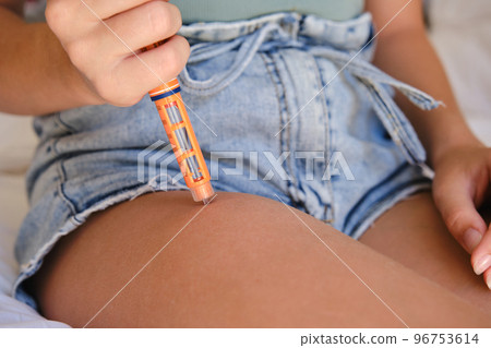 Close-up of a child with diabetes giving a subcutaneous injection of insulin in his leg. 96753614