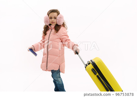 Fashionable little child, traveler girl in pink down coat, blue jeans and fluffy earmuffs, traveling abroad for winter holidays, walking with suitcase on white background. Journey Travel Tourism Trip Fashionable little child, traveler girl in pink down coat, blue jeans and fluffy earmuffs, traveling abroad for winter holidays, walking with suitcase on white background. Journey Travel Tourism Trip 96753878