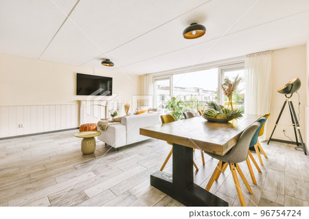 Shabby wooden table with chairs and vase located near comfortable couch against light walls with decorations and TV in modern apartment 96754724