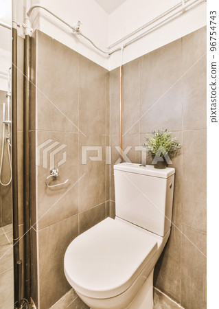 Interior of narrow restroom with sink and wall hung toilet with white walls and checkered floor 96754743