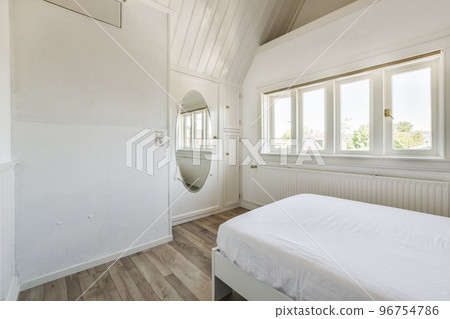 Modern home interior design of small mansard bedroom with white walls and soft cozy bed in daylight 96754786