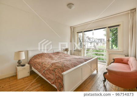 Comfortable bed with bedclothes and bedside table with lamp placed near window and balcony door in light bedroom at home Comfortable bed with bedclothes and bedside table with lamp placed near window and balcony door in light bedroom at home 96754873