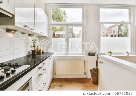 Fragment of interior of light narrow home kitchen with minimalist style white furniture with sink and stove 96755083