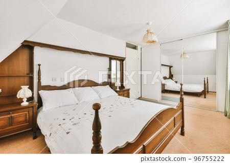 Home interior design of bedroom with bed and wooden wardrobe placed in corner near window in modern apartment 96755222