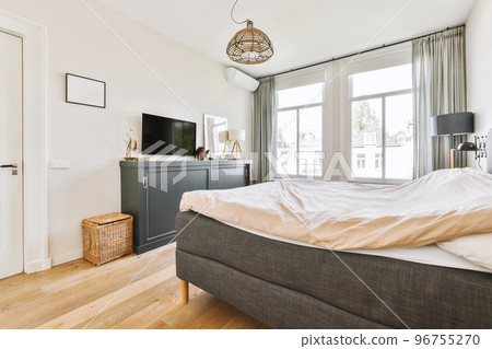 Home interior design of bedroom with bed and wooden wardrobe placed in corner near window in modern apartment 96755270