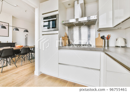 Fragment of interior of light narrow home kitchen with minimalist style white furniture with sink and stove 96755461