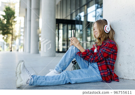 Young smiling beautiful hipster happy teen girl in city street,speaking on smartphone,headphones, jeans, backpack, positive, spring trend, urban teenage style 96755611