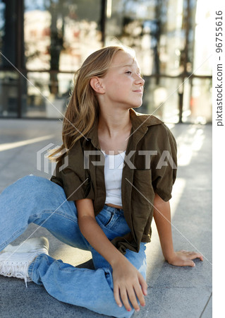 Portrait of teenage girl sitting on floor, urban street, sunlight 96755616