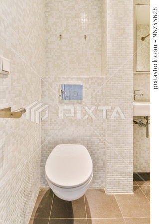 Modern flush toilet and ceramic sink installed on white tiled walls near mirror and towel in small restroom at home Modern flush toilet and ceramic sink installed on white tiled walls near mirror and towel in small restroom at home 96755628