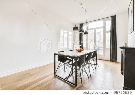 Wooden table with vase of flowers under black pendant lamp in modern living room with sofa near window Wooden table with vase of flowers under black pendant lamp in modern living room with sofa near window 96755629