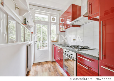 Fragment of interior of light narrow home kitchen with minimalist style red furniture with sink and stove 96755666