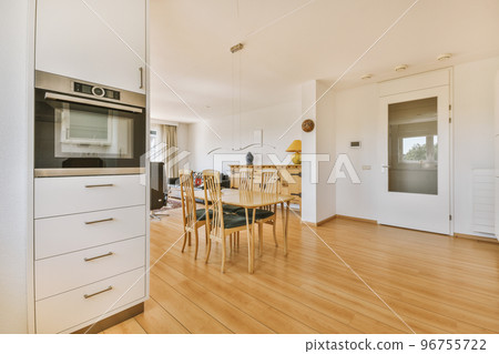 Contemporary minimalist style interior design of light studio apartment with wooden table and chairs in dining zone between open kitchen and living room with white walls and parquet floor Contemporary minimalist style interior design of light studio apartment with wooden table and chairs in dining zone between open kitchen and living room with white walls and parquet floor 96755722