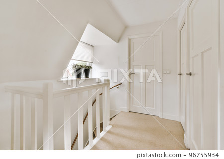 Closed white door of room located near framed pictures and stylish lamp on top of stairway at home 96755934