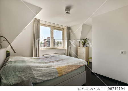 Modern home interior design of small mansard bedroom with white walls and soft cozy bed and minimalist style shelves in daylight with illumination 96756194
