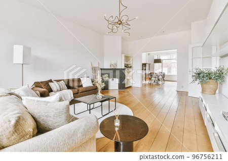 Comfortable sofa with soft cushions located under stylish chandelier in spacious light living room with arch 96756211