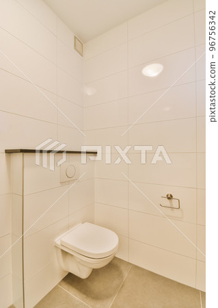 Flush toilet located between sink and shower in small tiled bathroom of contemporary apartment 96756342