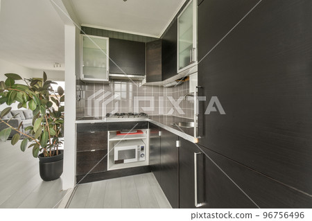 Dark brown cabinets with wooden counter of modern kitchen and dining table set in living room of apartment Dark brown cabinets with wooden counter of modern kitchen and dining table set in living room of apartment 96756496