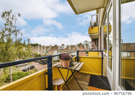 Narrow brick balcony with metal railings, wooden chair and door with glass leads to the kitchen Narrow brick balcony with metal railings, wooden chair and door with glass leads to the kitchen 96756796
