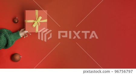 Female hands with christmas red gift box, golden bow on the red background. Green sweater. New Year concept. Winter holidays and presents. Surprise delivery Female hands with christmas red gift box, golden bow on the red background. Green sweater. New Year concept. Winter holidays and presents. Surprise delivery 96756797