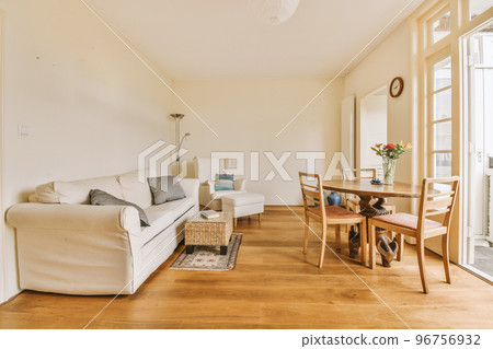 Shabby wooden table with chairs and vase located near comfortable couch against light walls with decorations and TV in modern apartment 96756932
