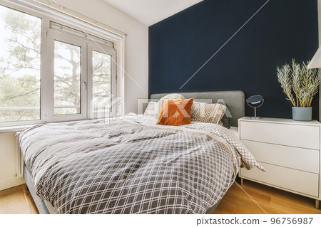 Home interior design of bedroom with bed and wooden wardrobe placed in corner near window in modern apartment 96756987