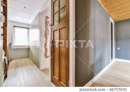 Narrow corridor with white walls and doors leading to spacious room with windows and parquet floor in modern apartment 96757045