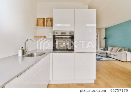 Fragment of interior of light narrow home kitchen with minimalist style white furniture with sink and stove Fragment of interior of light narrow home kitchen with minimalist style white furniture with sink and stove 96757179