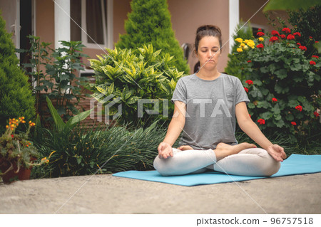 Concentrated woman sitting in lotus position yoga at summer garden park plants and blossom flowers 96757518