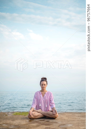 Yoga woman meditation prayer hands namaste overhead lotus position sitting sand sky beach landscape 96757664