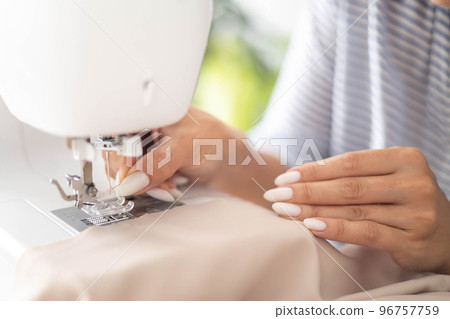 Woman dressmaker tailor thread needle at electric sewing machine fabric clothes manufacture closeup Woman dressmaker tailor thread needle at electric sewing machine fabric clothes manufacture closeup 96757759