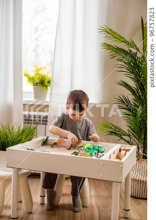 Cute male kid playing sensory box dinosaur world at comfortable home living room Cute male kid playing sensory box dinosaur world at comfortable home living room 96757823