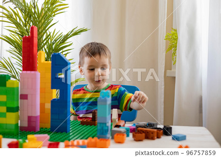 Confident male baby constructing tower with multicolored plastic pieces assembling house on table Confident male baby constructing tower with multicolored plastic pieces assembling house on table 96757859