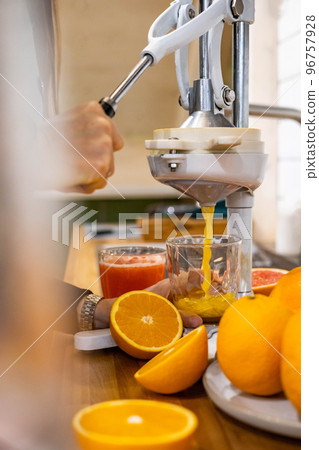 Closeup woman hand holding glass under flow of detox healthy orange juice use citrus press 96757928