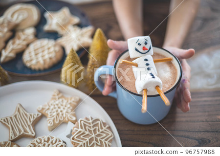 Little cute girl plays with knitted snowmen and eats gingerbread and drinks cocoa with marshmallows. 96757988