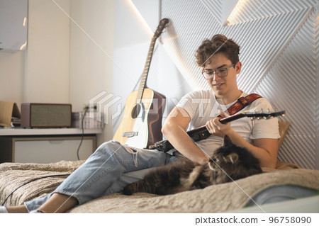 Cute cat relaxing near male playing electric guitar art hobby on couch at home 96758090