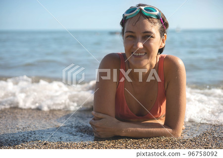 Portrait laughing tanned woman in goggles bikini pebble beach wave foamy sea water summer vacation 96758092