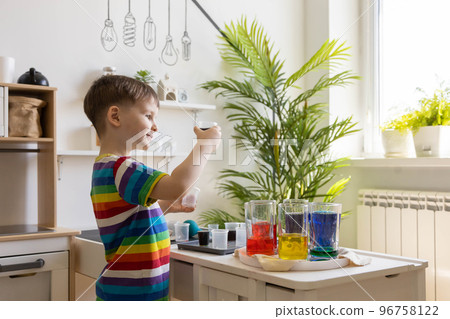 Cute baby boy learning mixing different colors with water and paint in containers. Early development 96758122