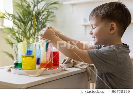 Cute baby boy learning mixing different colors with water and paint in containers. Early development 96758139